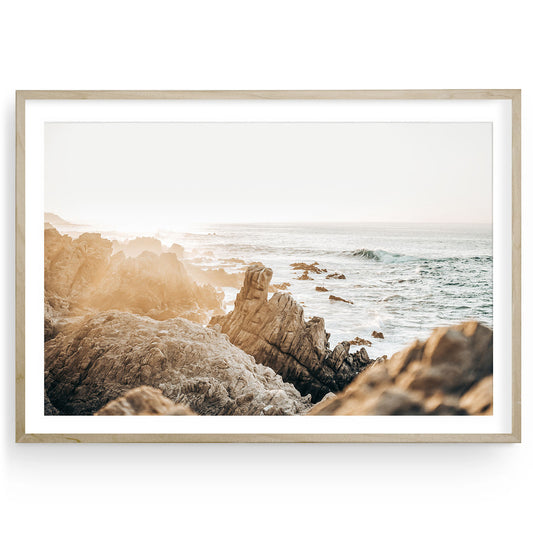 Framed coastal sunset print featuring rugged beige shoreline, boho beach rocks, and soft neutral tones — fine art wall decor for calming interiors.